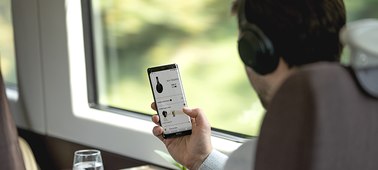    A male on the train wearing the Sony WH-1000XM3 changing headphone setting on his mobile phone